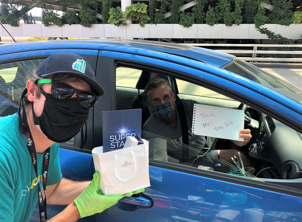 Jack Hughes, Travel Oregon, in his car holding a sign that says "Thank you! Stay Safe." Walt Marchbanks in PPE is handing him his PDX Excellence in Service award.