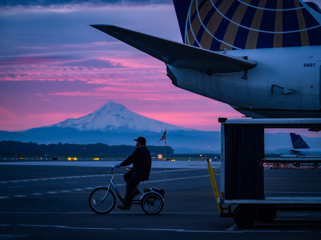 An electrician rides on his bicycle at PDX with Mt. Hood in the background