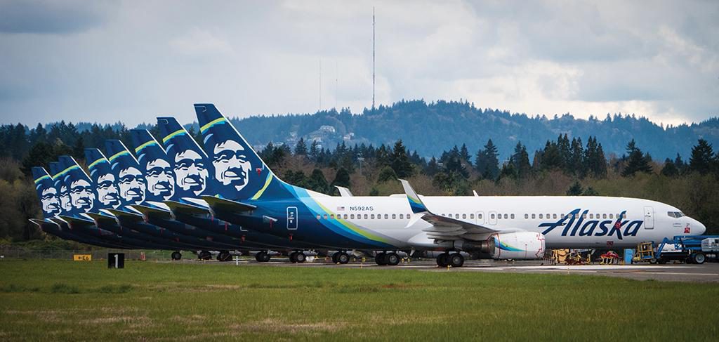 Eight Alaska Airlines planes are parked along a closed runway at PDX
