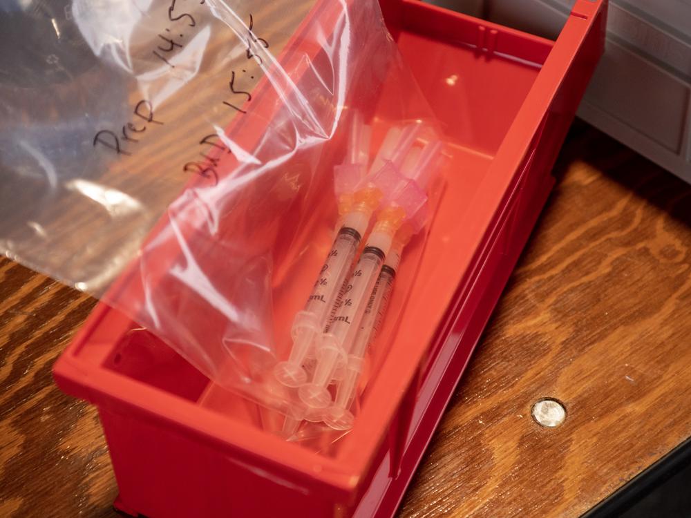 Four vaccine shot vials are in a bag and placed into a red box to be delivered to a vaccinator