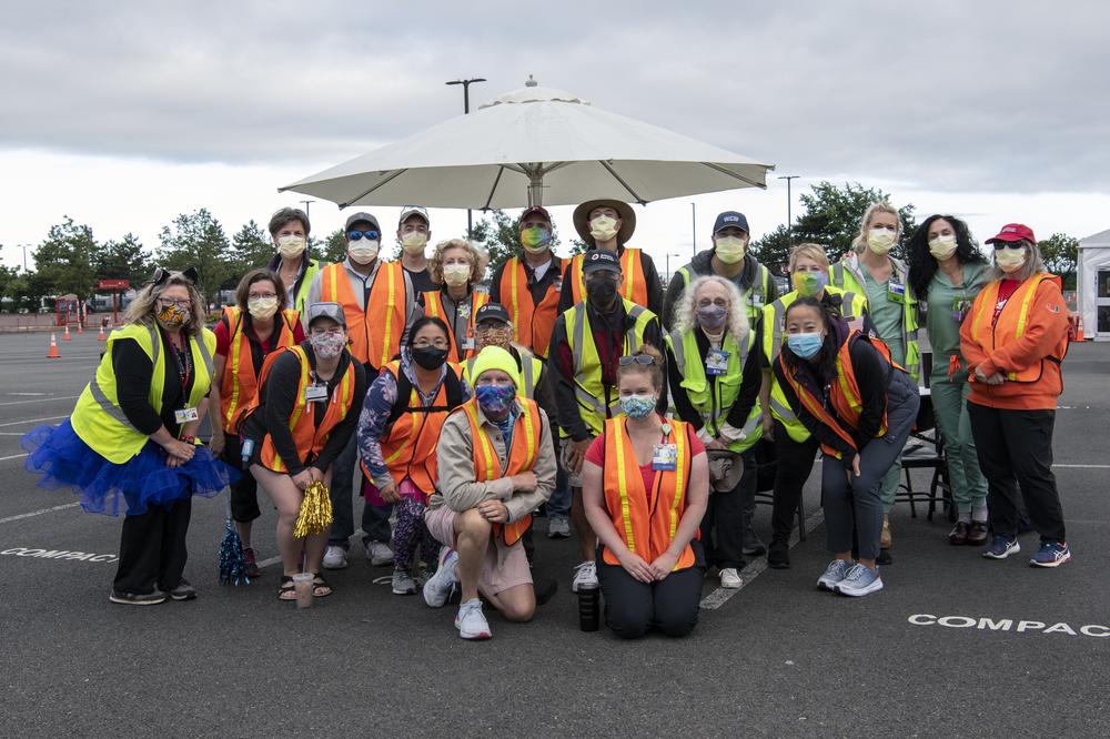 A group of volunteers stand and pose for a photo, wearing safety vests.