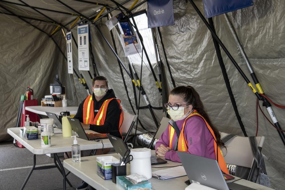 A woman and a man in orange safety vests sit inside a tent that was used for the PDX Red Lot vaccine clinic staff and volunteer check-in.