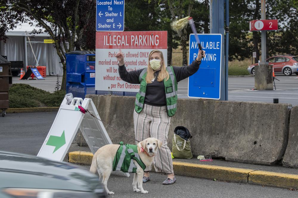 A woman and a dog, both with green vests on, wave a truck into the PDX Red Lot