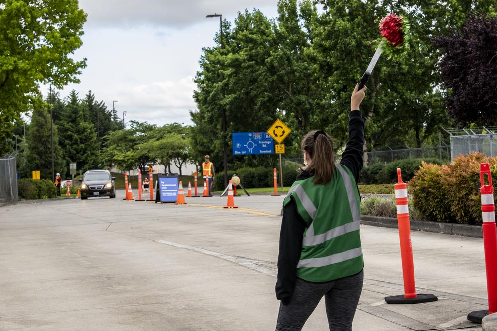 A woman waves a pom pom to welcome a truck into the PDX Red Lot vaccine clinic.