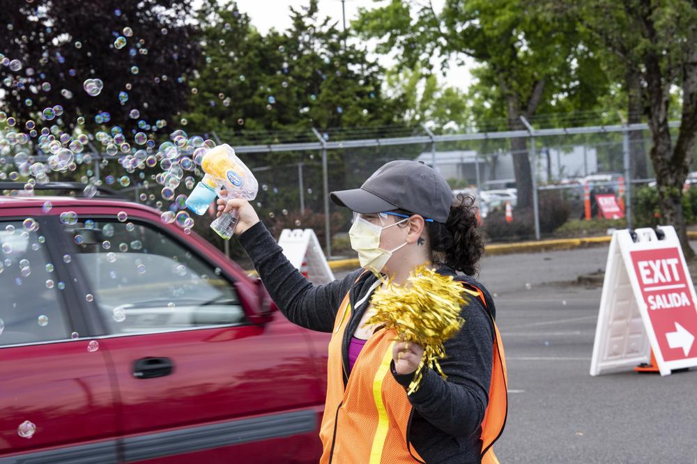 A woman with an orange safety vests sprays a bubble sprayer and holds a pom pom to celebrate people getting vaccinated.