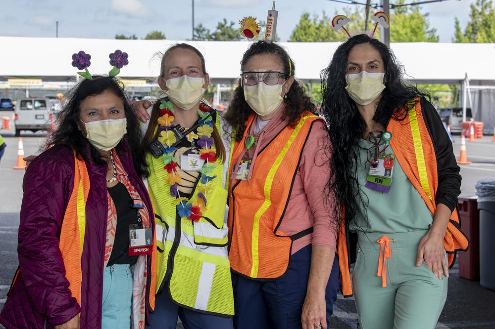 Four OHSU staff members in orange and yellow safety vests and masks pose for a photo. They are wearing headbands and festive necklaces