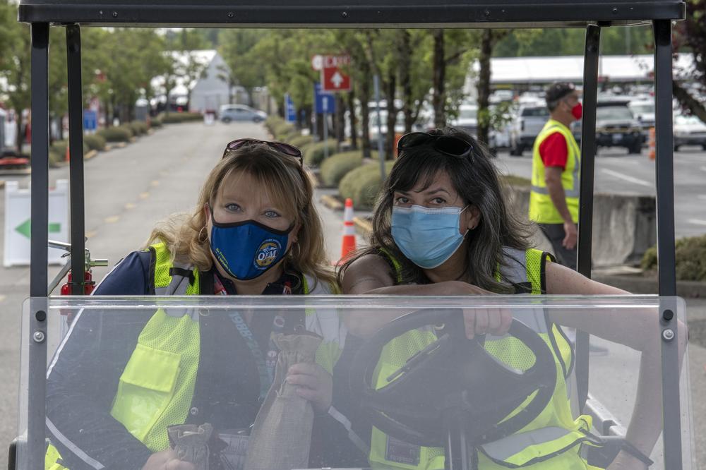 Two women pose while sitting in a golf cart at the PDX Red Lot. They are wearing masks.