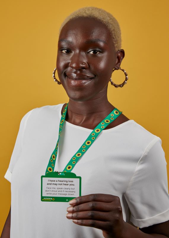 Woman wearing a sunflower lanyard with a card that reads "I have a hearing loss and may not hear you."