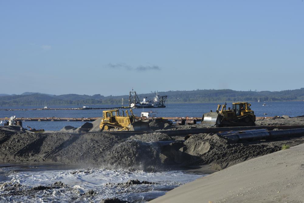 A bulldozer sits on a sandy beach moving sand around that was placed by the Dredge Oregon Navigation vessel